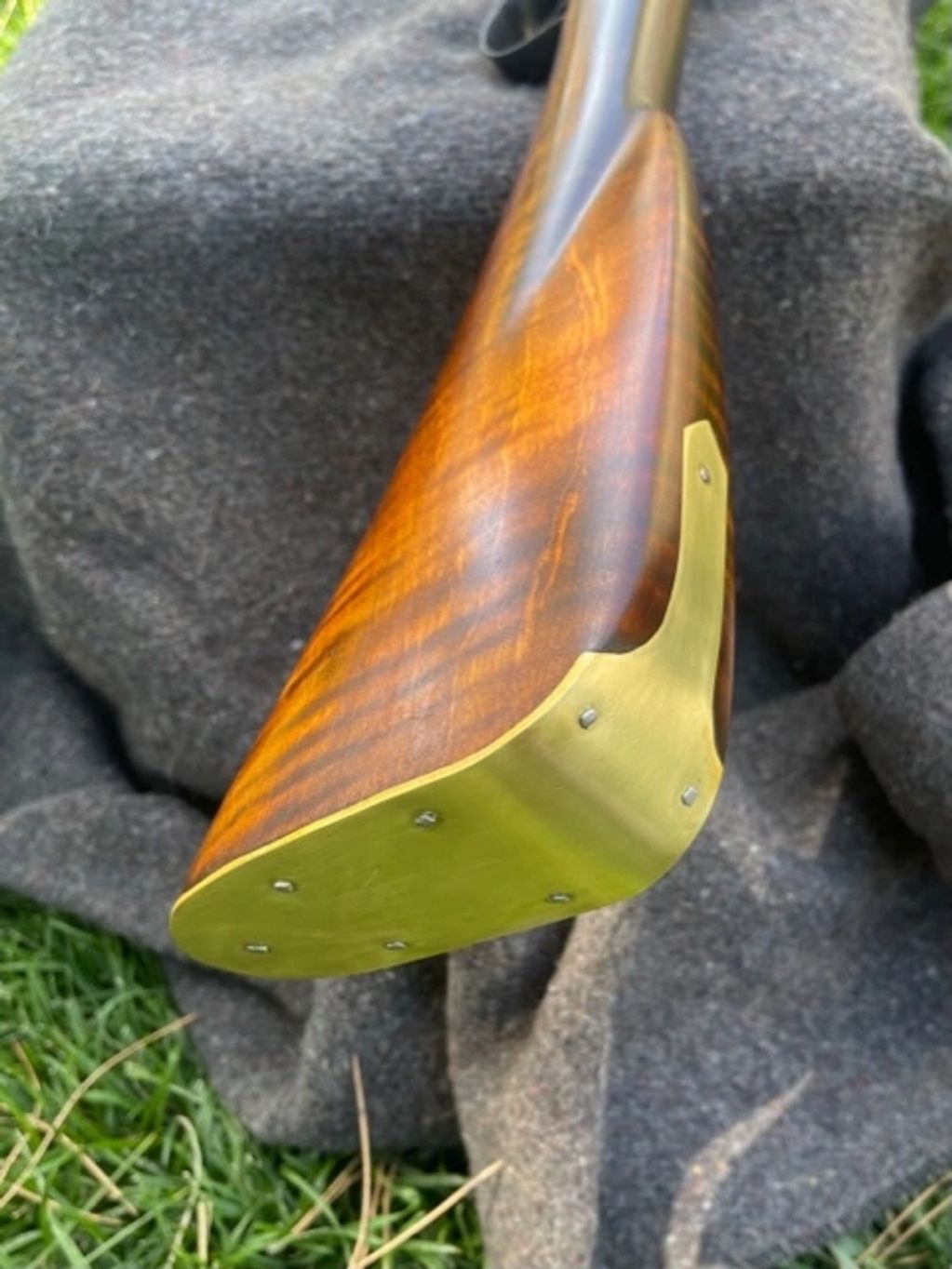 Close-up of a wooden rifle stock with brass buttplate on fabric.