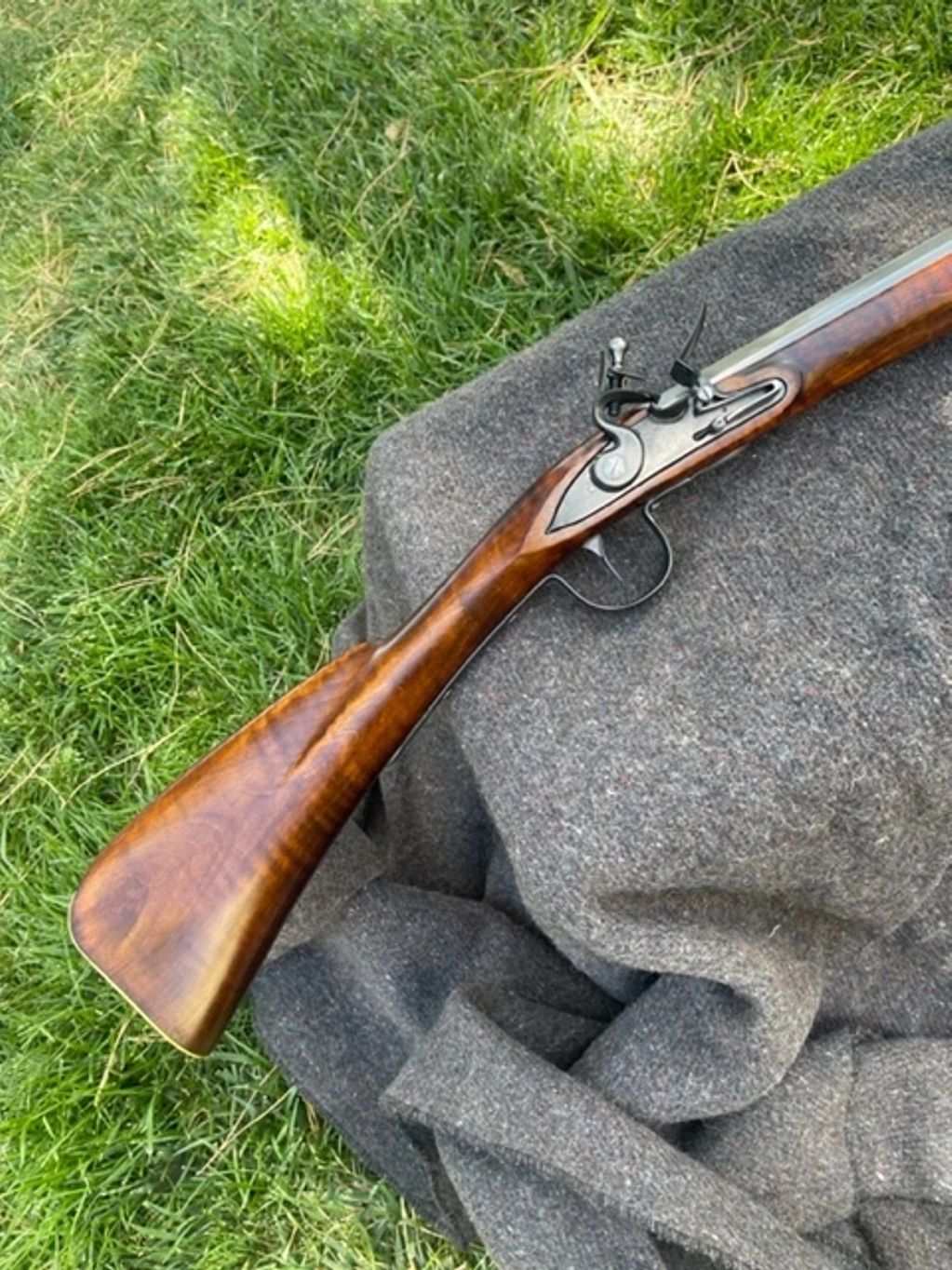 A vintage flintlock rifle resting on a gray fabric outdoors on grass.