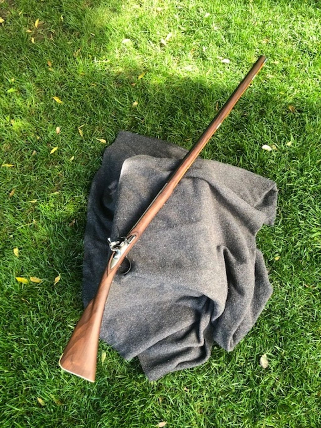 A vintage flintlock rifle rests on a gray cloth on green grass.