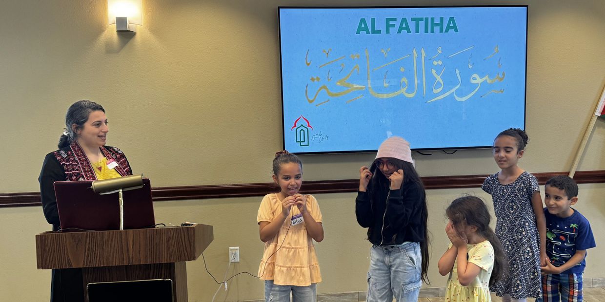 A woman teaches a group of children about Al Fatiha with a screen display.