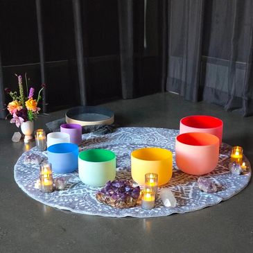 Colorful singing bowls arranged in a circle with candles and crystals.