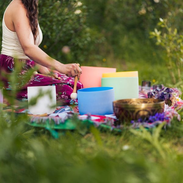 Woman playing colorful singing bowls outdoors in a serene natural setting.