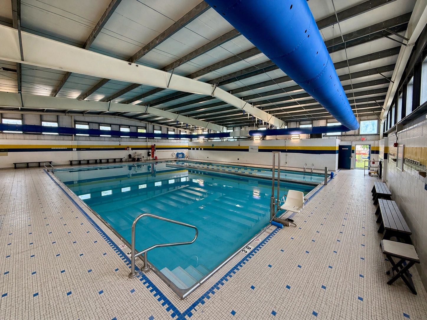 Indoor swimming pool with blue and white tiled floor and benches.