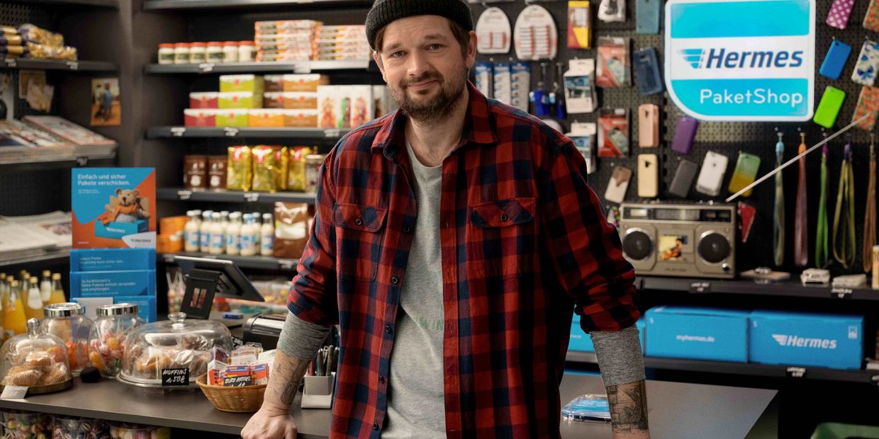 Ein Mitarbeiter steht vor dem Tresen eines Kiosk, der auch ein Hermes PaketShop ist.