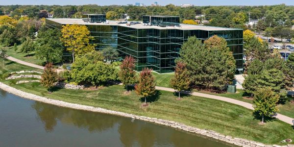 Modern office building by a waterbody surrounded by greenery.