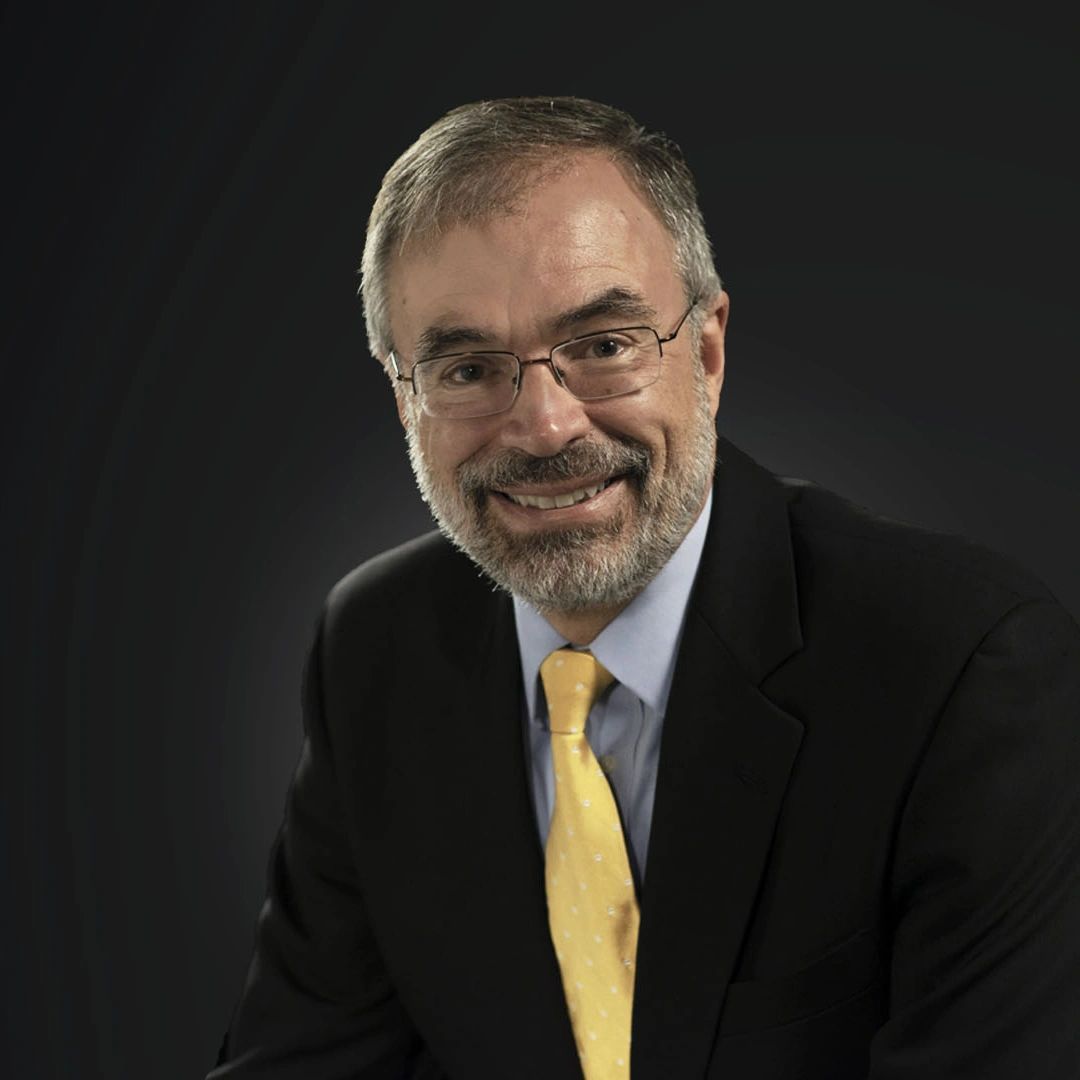Smiling man in suit with glasses and yellow tie.