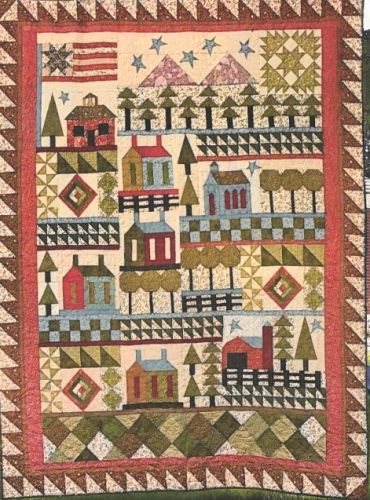 A colorful quilt featuring houses, trees, and geometric patterns.