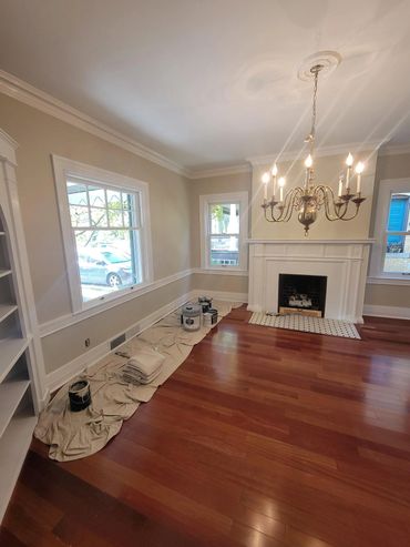 A bright room with wooden floors, fireplace, and painting supplies on drop cloths.