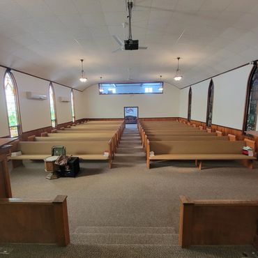 Interior view of a church with wooden pews and stained glass windows.