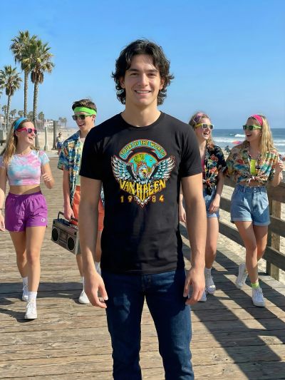 Young man in black Van Halen t-shirt with friends on beach boardwalk.