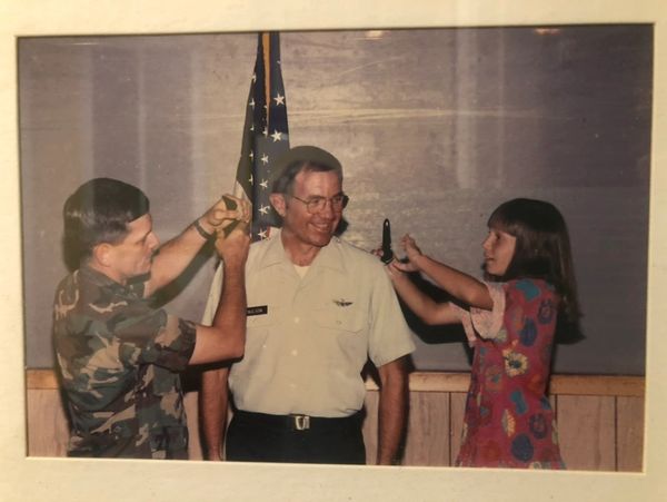 Two people pinning badges on a uniformed man smiling.