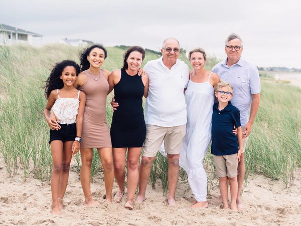 Family group posing on sandy beach with grass background.