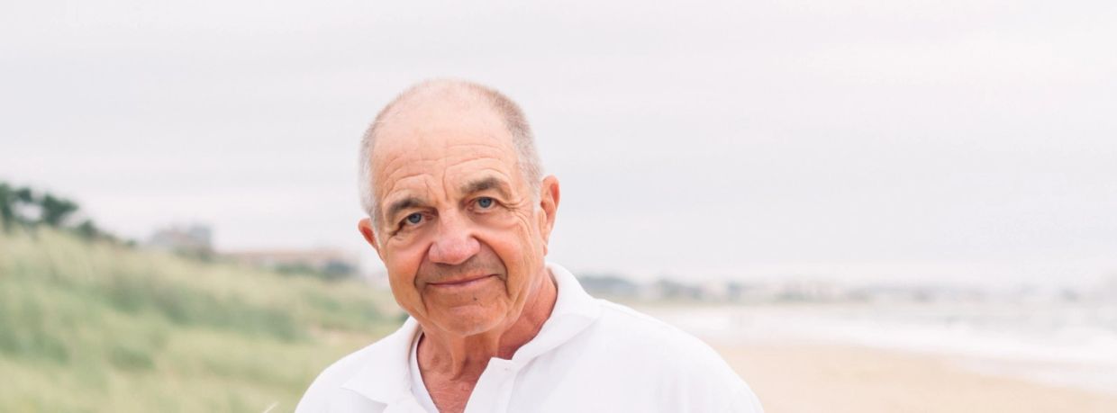Elderly man smiling outdoors on a beach.