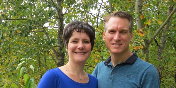 Smiling couple outdoors with green trees in background.