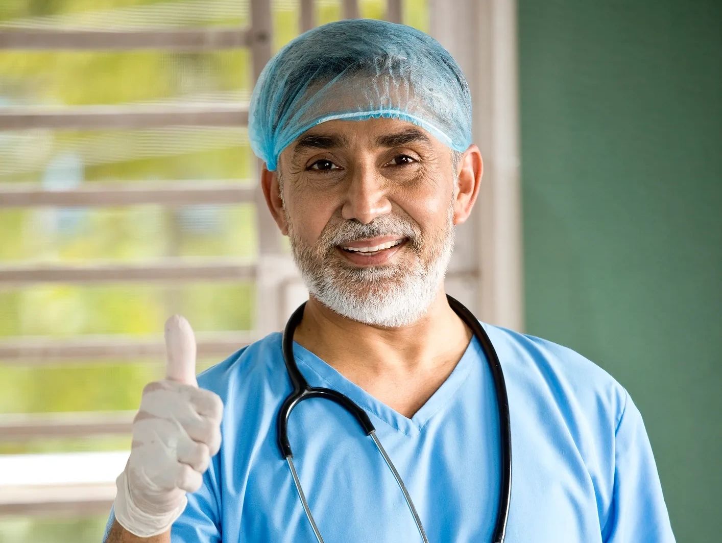 Smiling male doctor in blue scrubs gives a thumbs up.