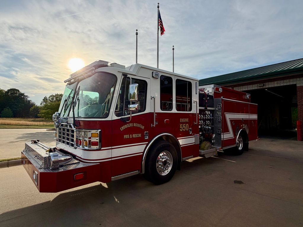 A red and white fire truck parked outside a fire station at sunset.