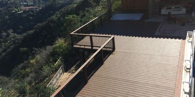 Spacious wooden balcony overlooking a forested hillside with a tiled roof patio.