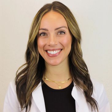 Smiling woman with long wavy hair wearing a white coat and necklace.