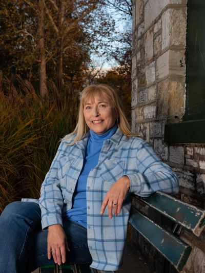 Woman in a blue plaid jacket sitting on a green bench outdoors.