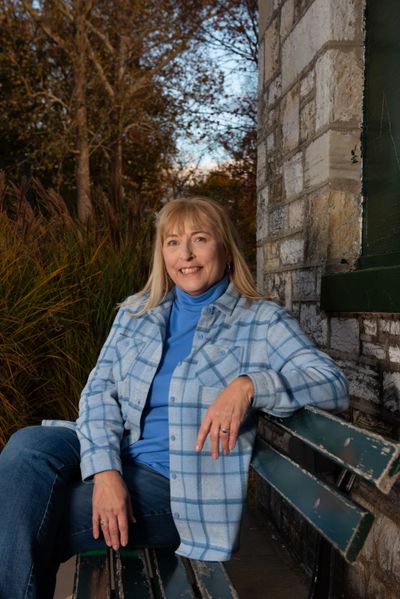 Woman in a blue plaid jacket sitting on a green bench outdoors.