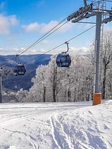 Ski lift carrying passengers over a snowy mountain landscape with frosted trees.