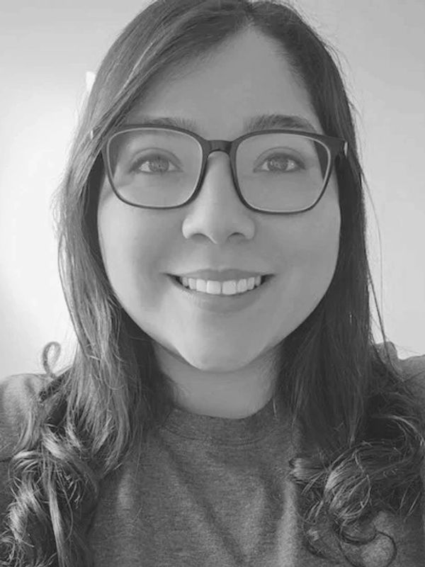 Smiling woman with glasses and curly hair in a grayscale photo.