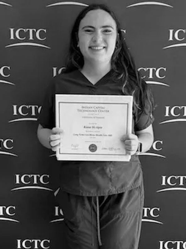 Young woman proudly holding a certificate from ICTC.