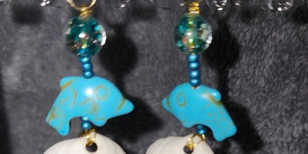 Earrings with Blue dolphins dangling from blue beads jumping over a white seashell from the Gulf