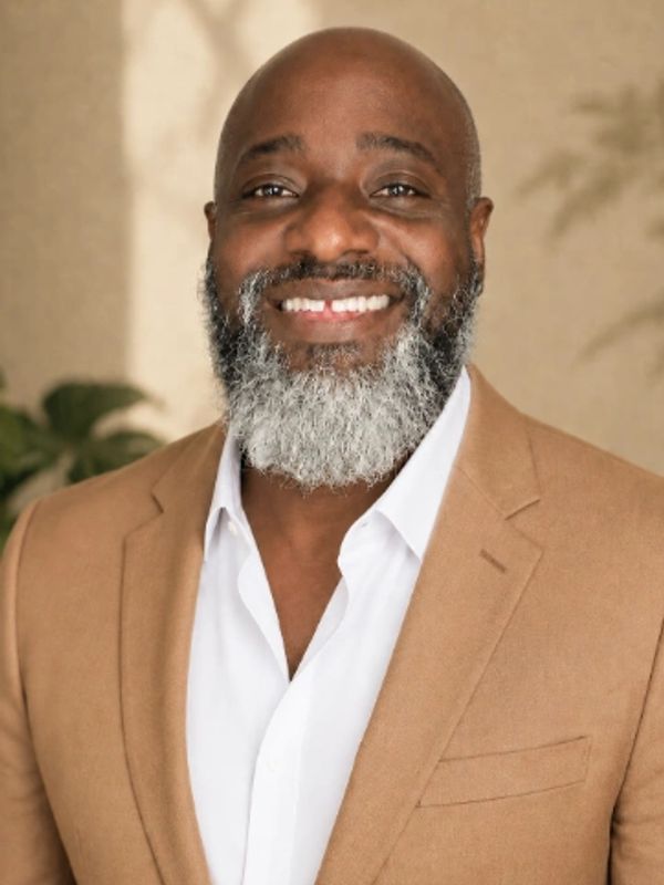 Smiling man with a gray beard in a tan blazer.