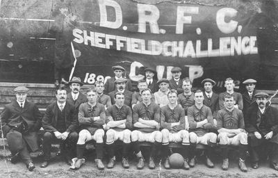 Black and white photo of a vintage rugby team posed before the Sheffield Challenge Cup banner.