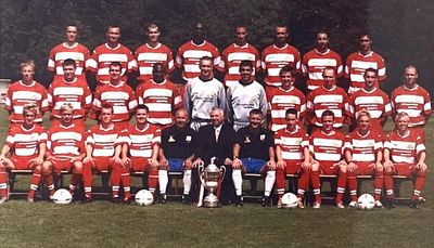 A soccer team posing with trophies on a field.