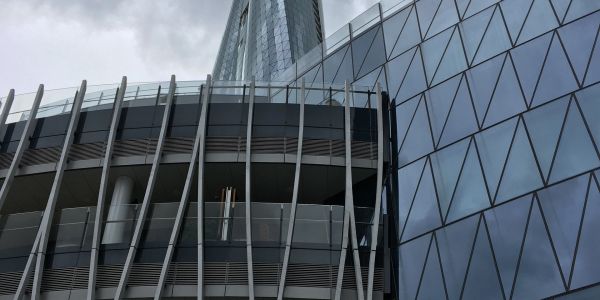 Modern glass skyscraper with unique structural design under cloudy sky.
