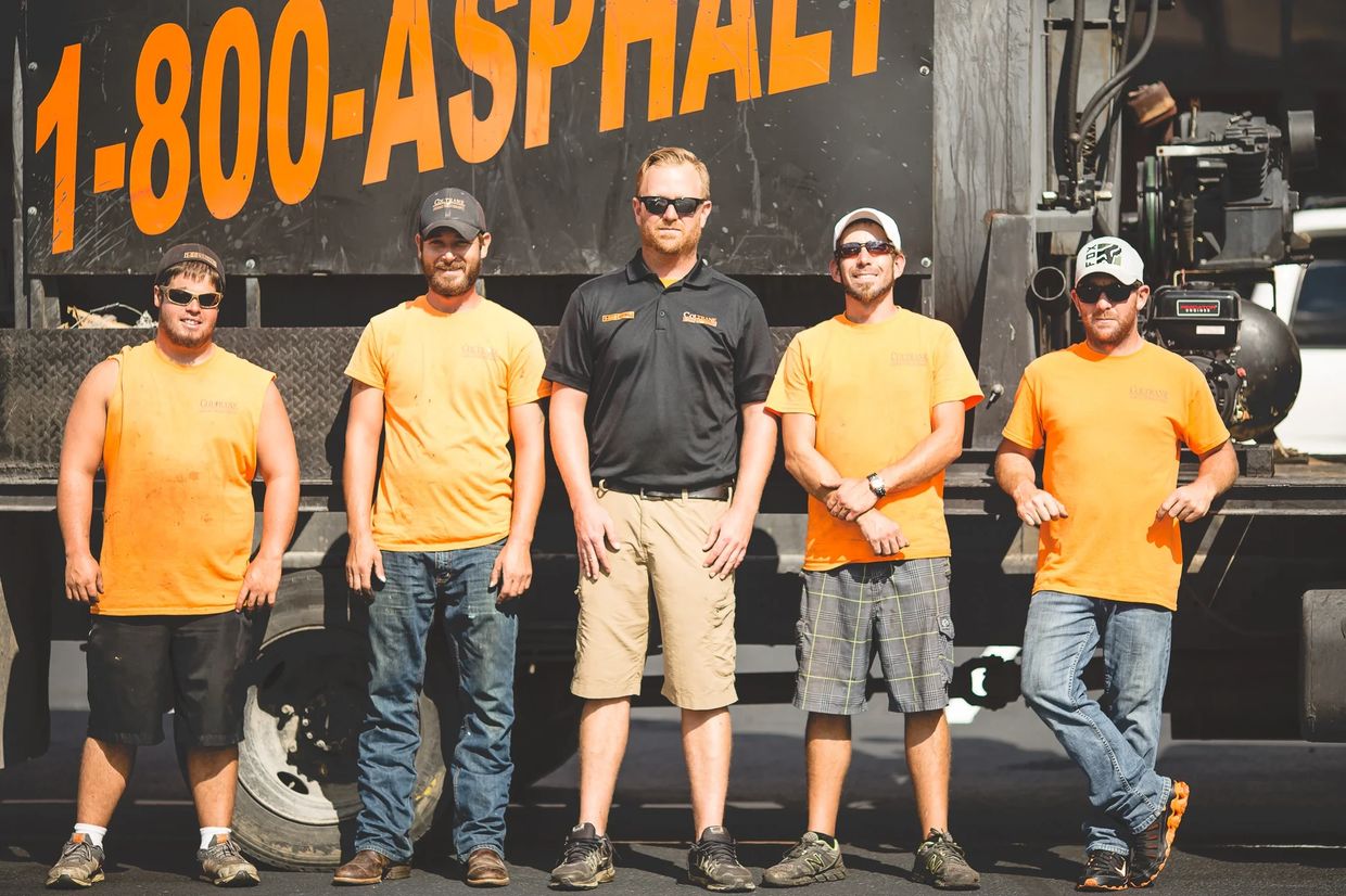 Five asphalt workers posing in front of a truck with a large "1-800-ASPHALT" sign.