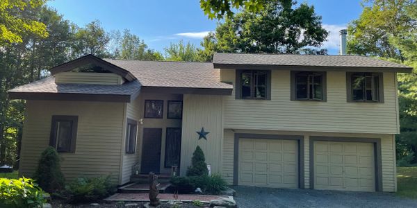 A beige split-level house with a two-car garage surrounded by trees.