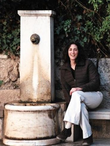 Woman sitting on a bench beside an old stone fountain outdoors.