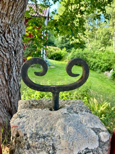 Wrought iron handle on stone pedestal in lush garden.