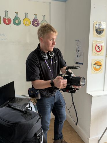 Man holding a professional camera in an indoor setting.