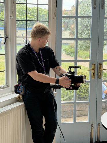 Person filming indoors with a camera near glass doors.