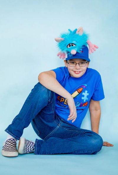 A boy wearing a blue shirt and hat with a playful blue puppet on top.