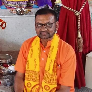 Man sitting in front of a Hindu altar with statues and offerings.