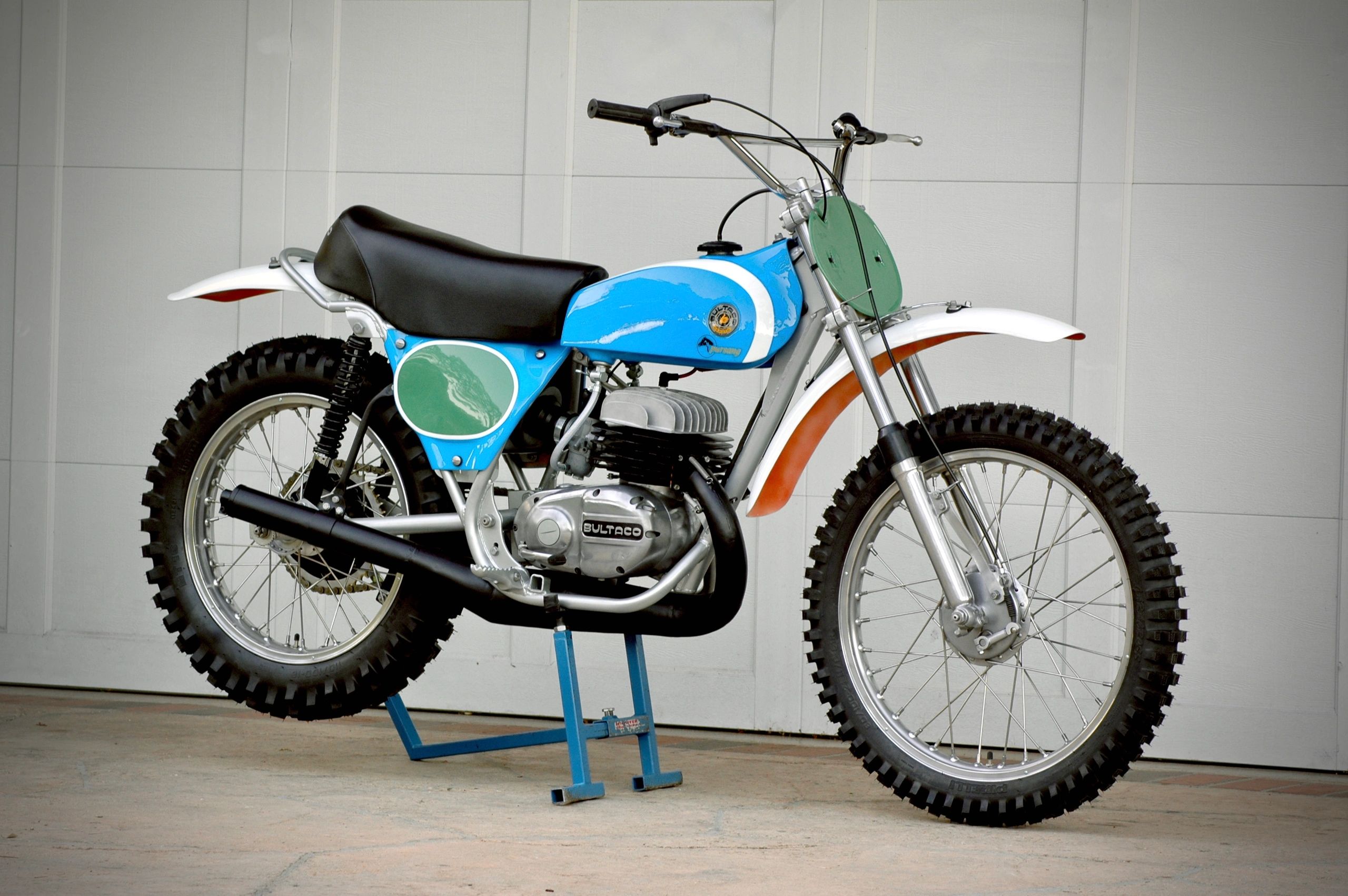 Vintage Bultaco dirt bike with blue and white paint and knobby tires.