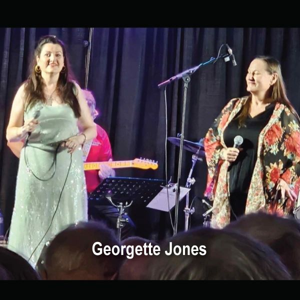 Two women performing on stage with microphones, one in a sparkly dress.
