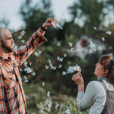 A couple in casual clothing blowing dandelions together in a garden during golden hour.