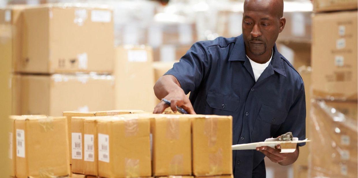 man in a warehouse checking a clipboard with boxes, supply chain economics, trading depots