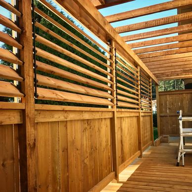 Sunlit wooden pergola with slatted fence panels and a chair on the deck.