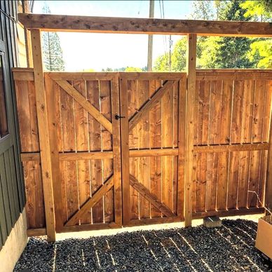 Wooden double gate attached to a wooden fence with gravel ground.