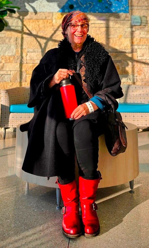 Smiling woman in red boots holding a red thermos, sitting indoors.