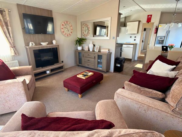 Cozy living room with beige sofas, burgundy cushions, and a wall-mounted TV above a fireplace.