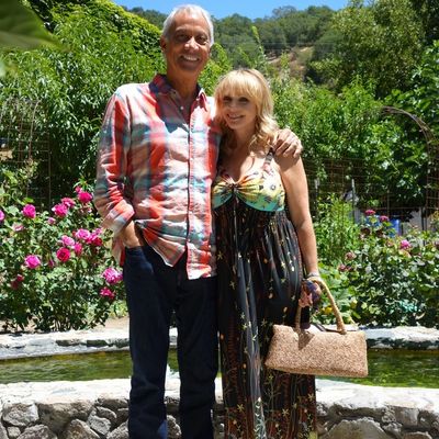 Couple posing happily in a garden with bright flowers and greenery.