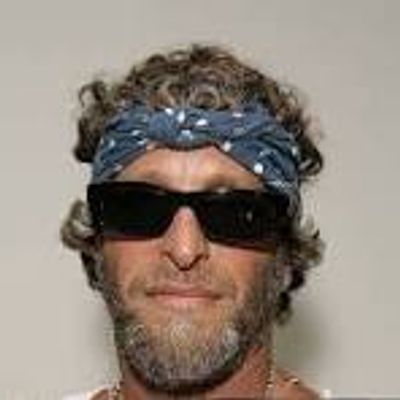 Man with curly hair wearing sunglasses and a blue bandana.